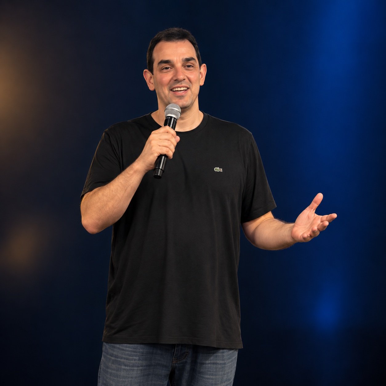 Victor Mirshawka Jr. com microfone e gesto de mão aberta, em retrato com fundo azul