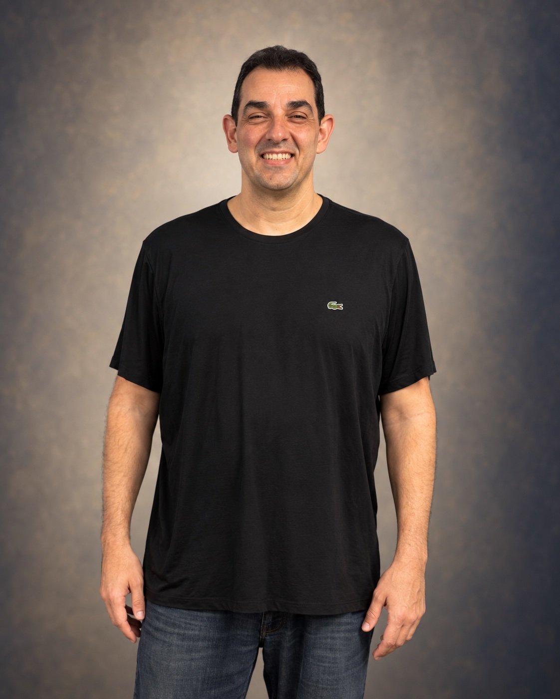Retrato de Victor Mirshawka Jr. sorrindo, de camiseta preta e fundo neutro